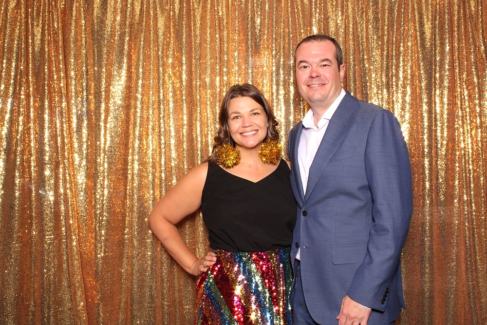 Couple at the Posed photo booth in front of a gold sequin backdrop, Austin