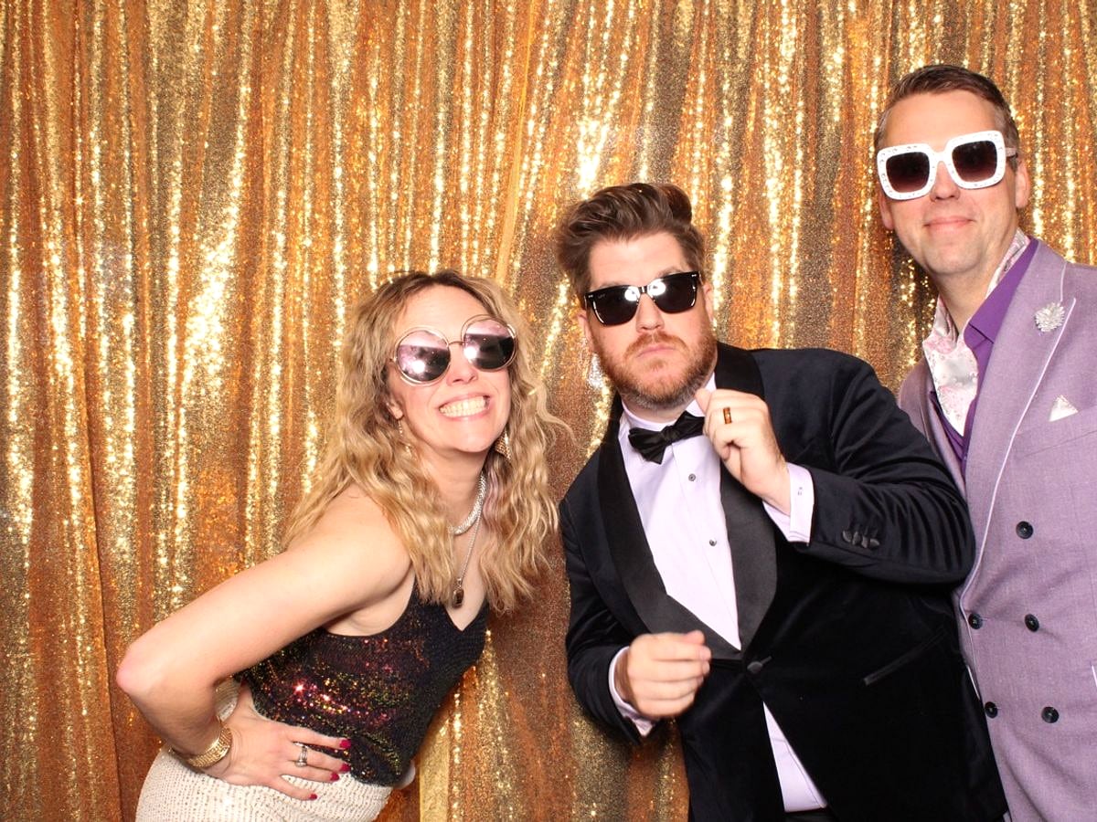 Group of friends in sunglasses laughing at the Posed photo booth, gold sequin backdrop, Austin